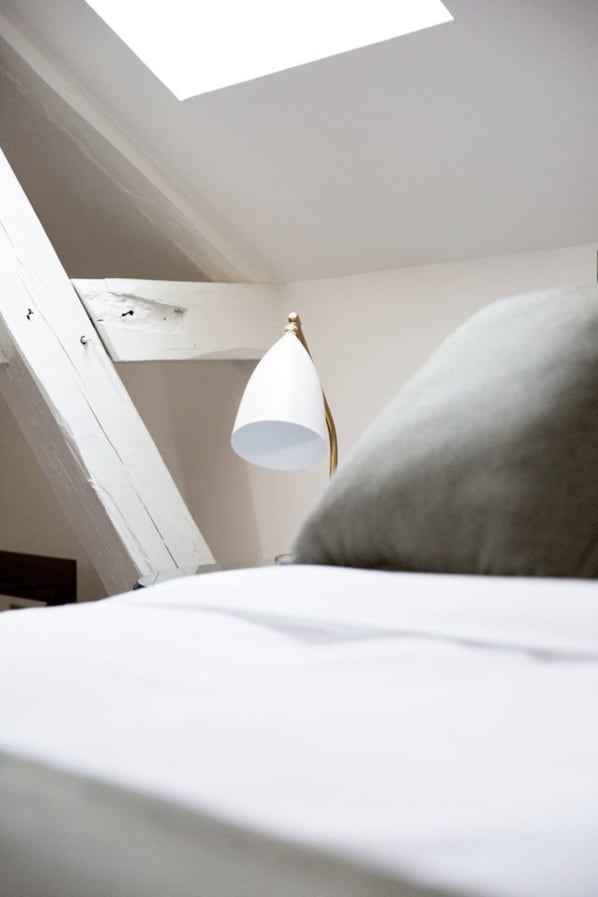 Un dormitorio con tragaluz, una lámpara blanca y una almohada gris.