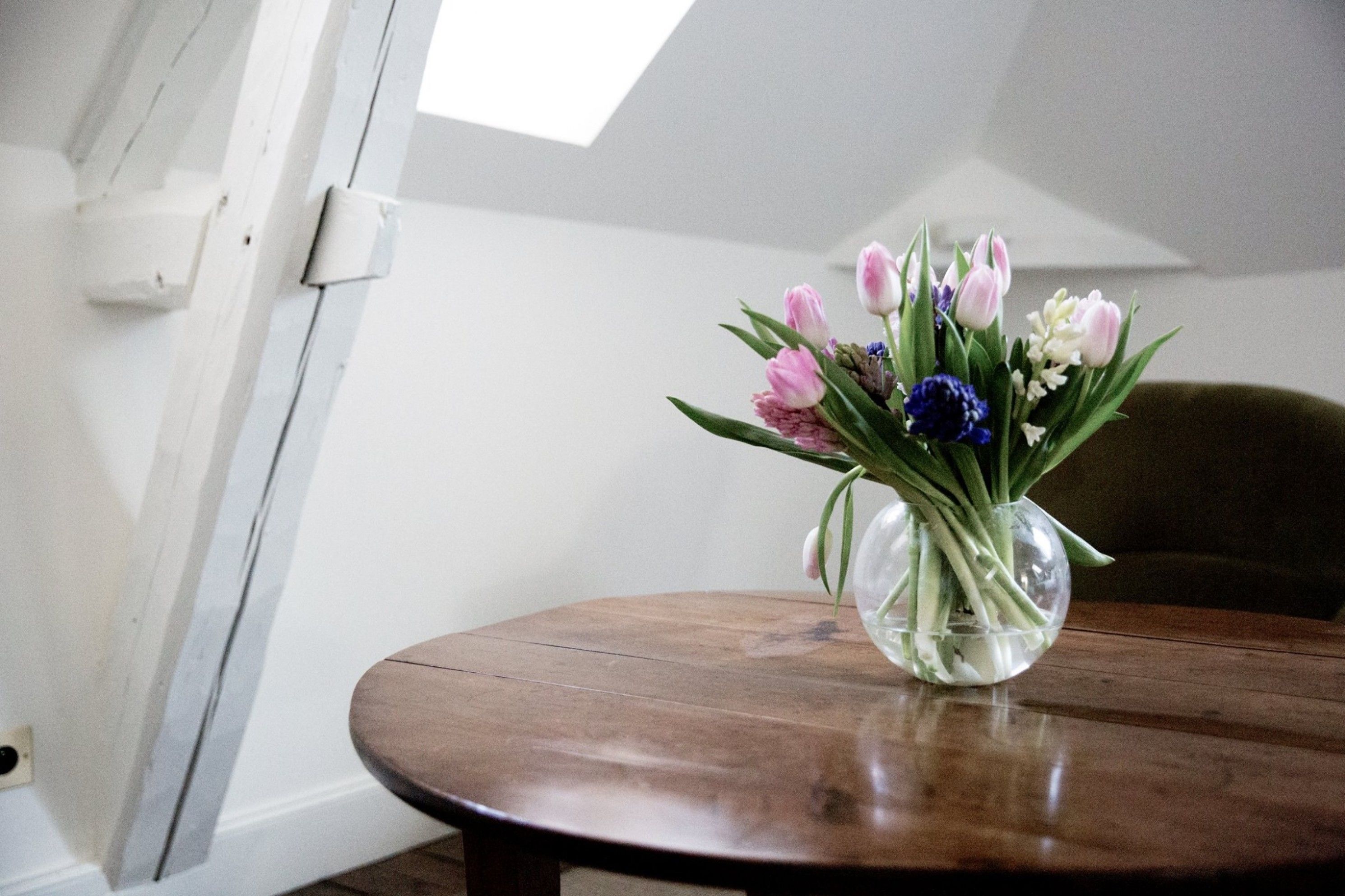 A round wooden table with a clear glass vase containing flowers.