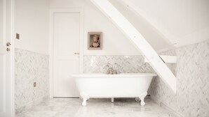 Un baño blanco con una bañera independiente, paredes con patrón de espiga y una puerta con un cuadro enmarcado.