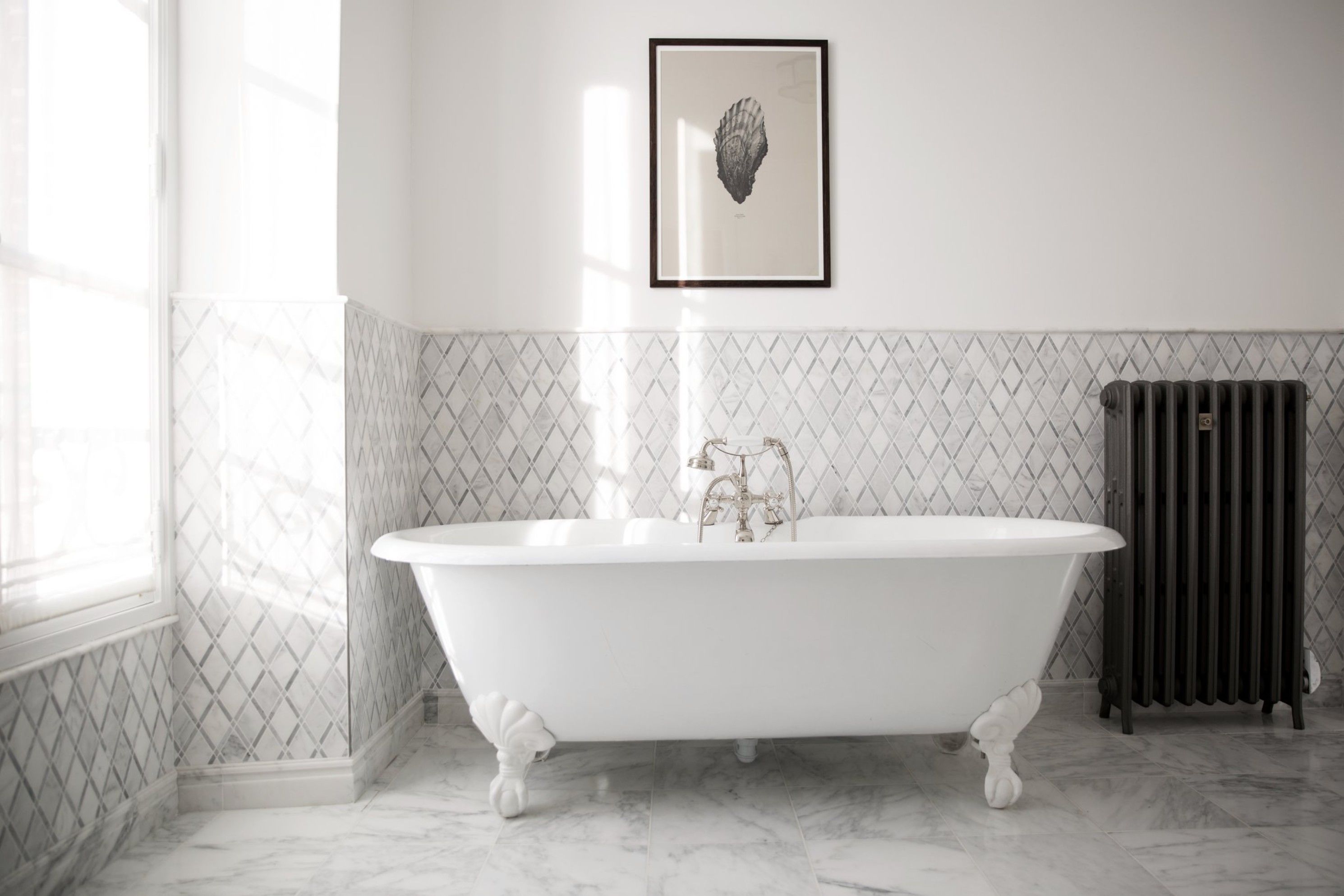 A bathroom with a freestanding bathtub, a radiator, and a framed artwork on the wall.