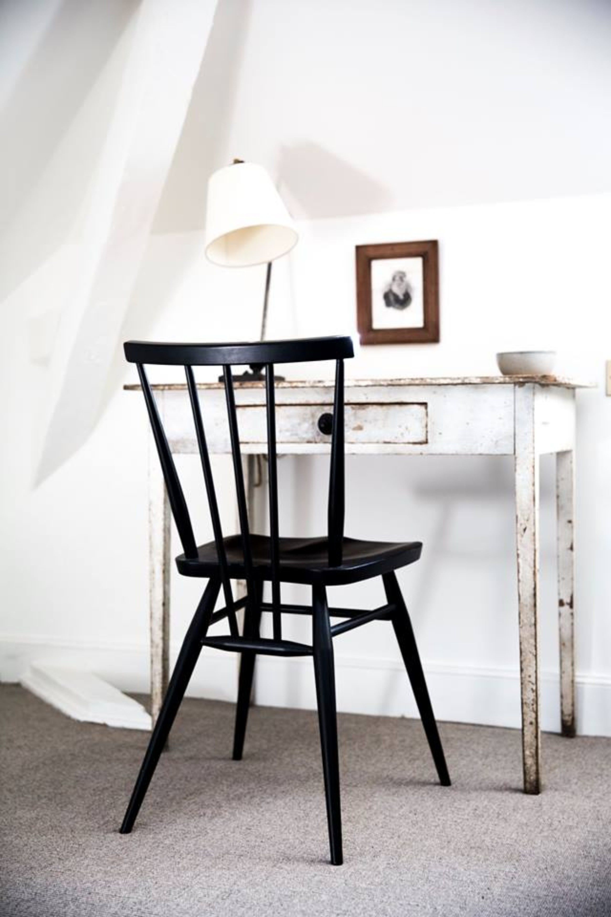 Een zwarte stoel met een witte lamp naast een witte tafel met een fotolijst.