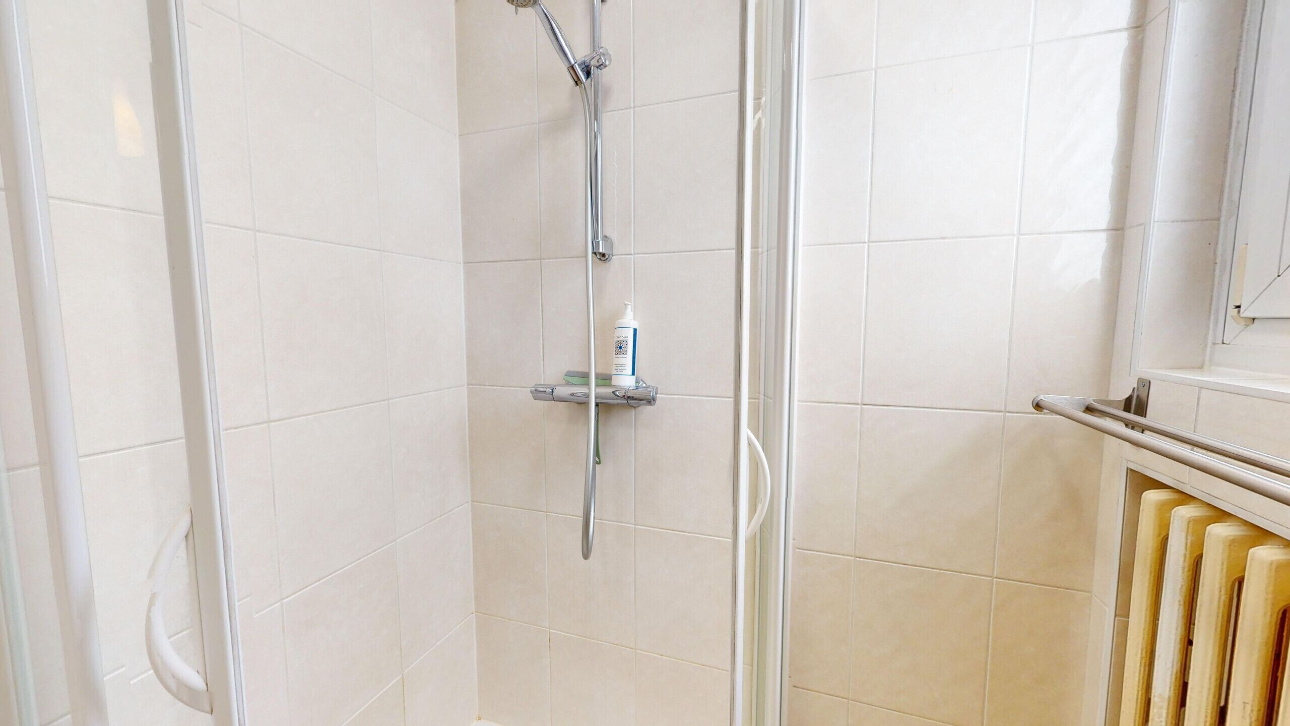 Une douche avec un pommeau de douche amovible, une bouteille de shampoing et un porte-serviettes.