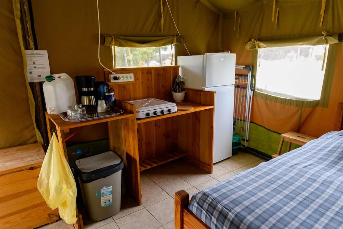 A compact kitchen with a stove, coffee maker, and refrigerator, a small trash bin, and a window overlooking greenery.