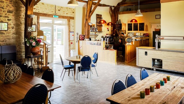 Un interior rústico con vigas de madera a la vista, una zona de bar y un espacio de estar con mesas y sillas.