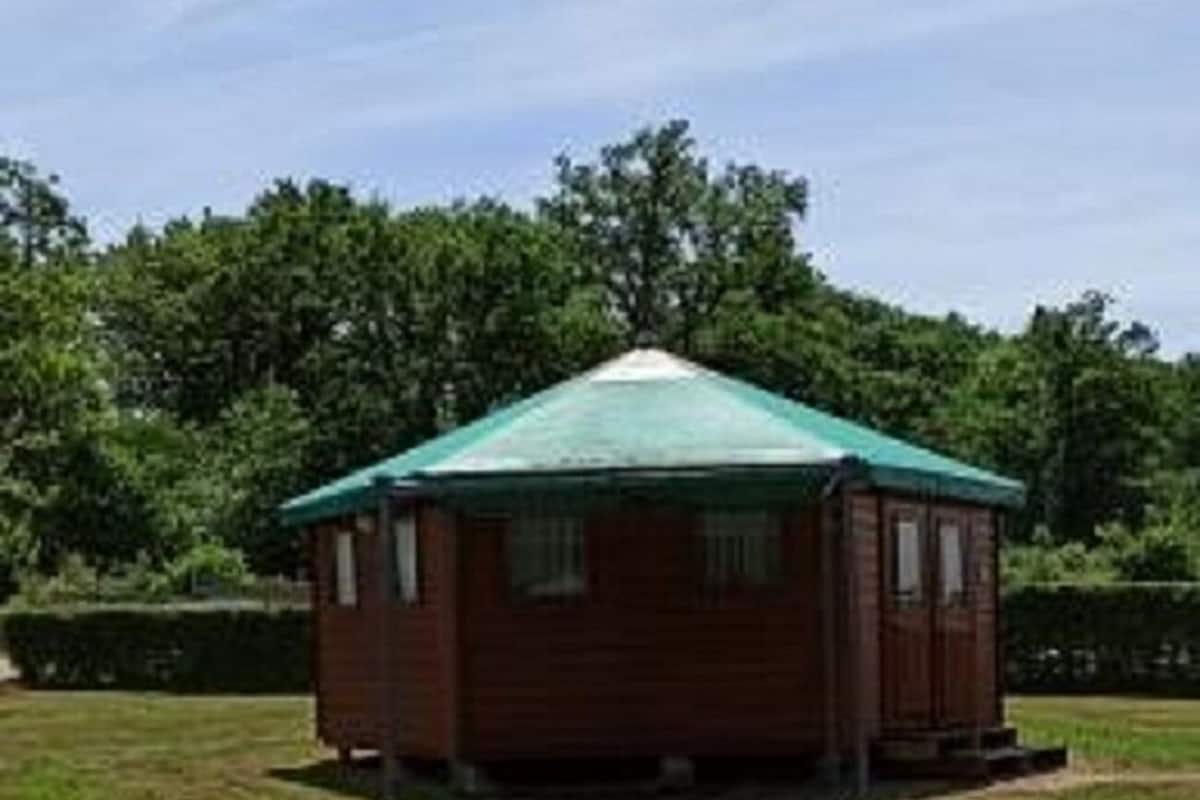 A small wooden cabin with a green roof, surrounded by a grassy field and trees.