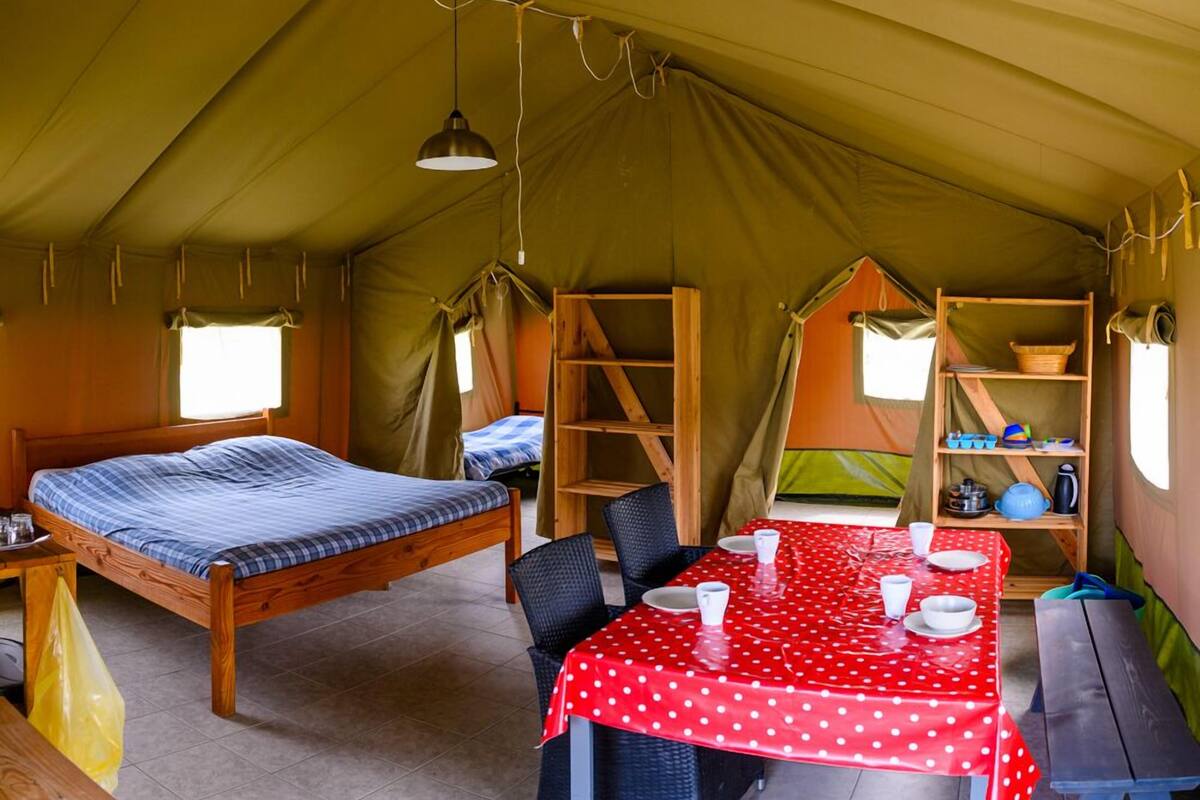 A tent with a bed, a dining table with chairs, and a shelf with kitchen items.