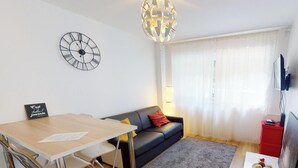 A modern living room with a wooden table, a black sofa, a grey rug, a clock on the wall, and a TV on a stand. - aux bons amis parlement orangerie  up to 4 (Strasbourg)