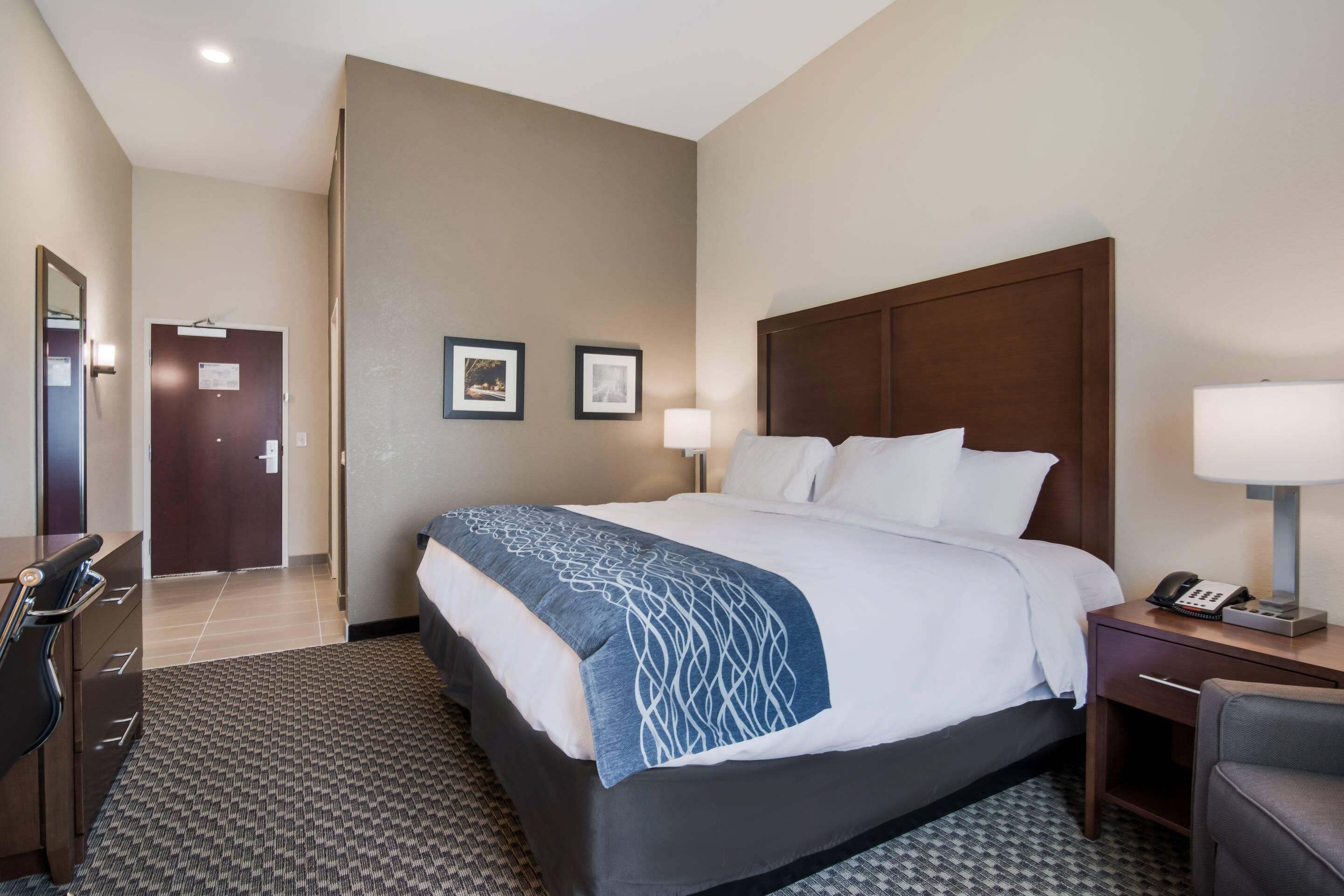 Una habitación de hotel con cama, escritorio, silla y puerta que da a otra habitación.