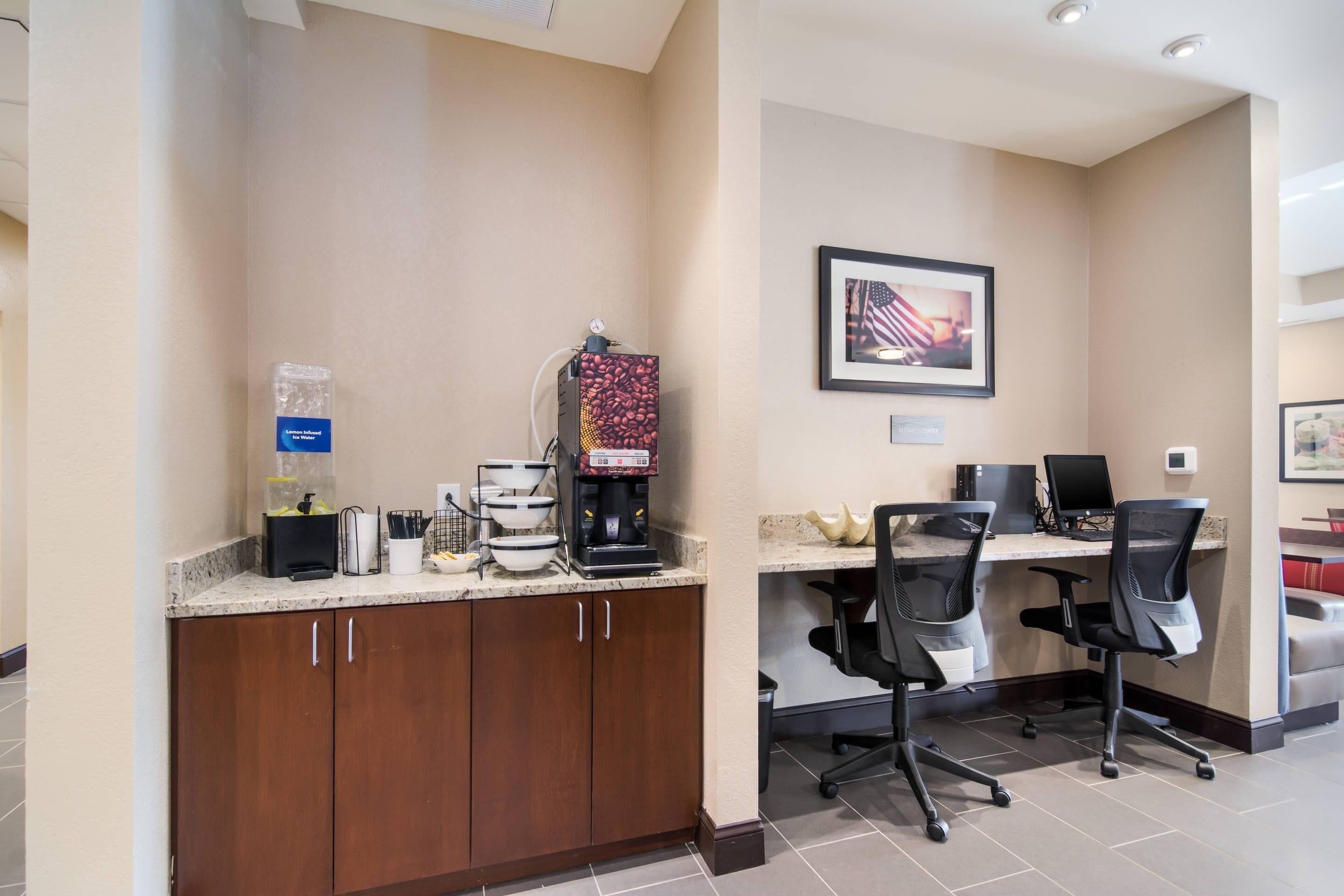 A hotel reception area with a coffee machine, a water dispenser, and a framed picture of the American flag on the wall.