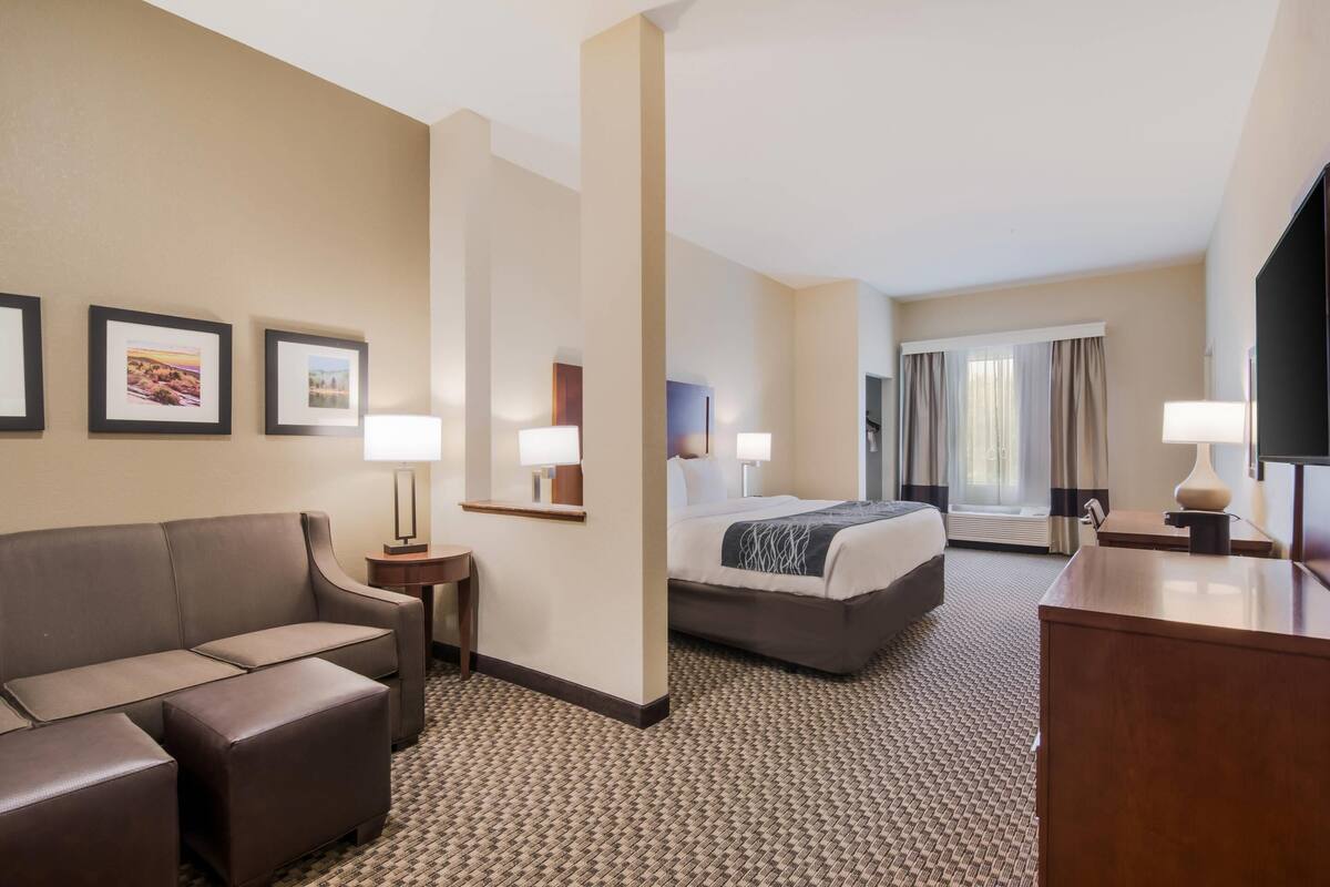 Ein Hotelzimmer mit einer Couch, einem Bett, einem Schreibtisch, einem Fernseher und gerahmten Bildern an der Wand.
