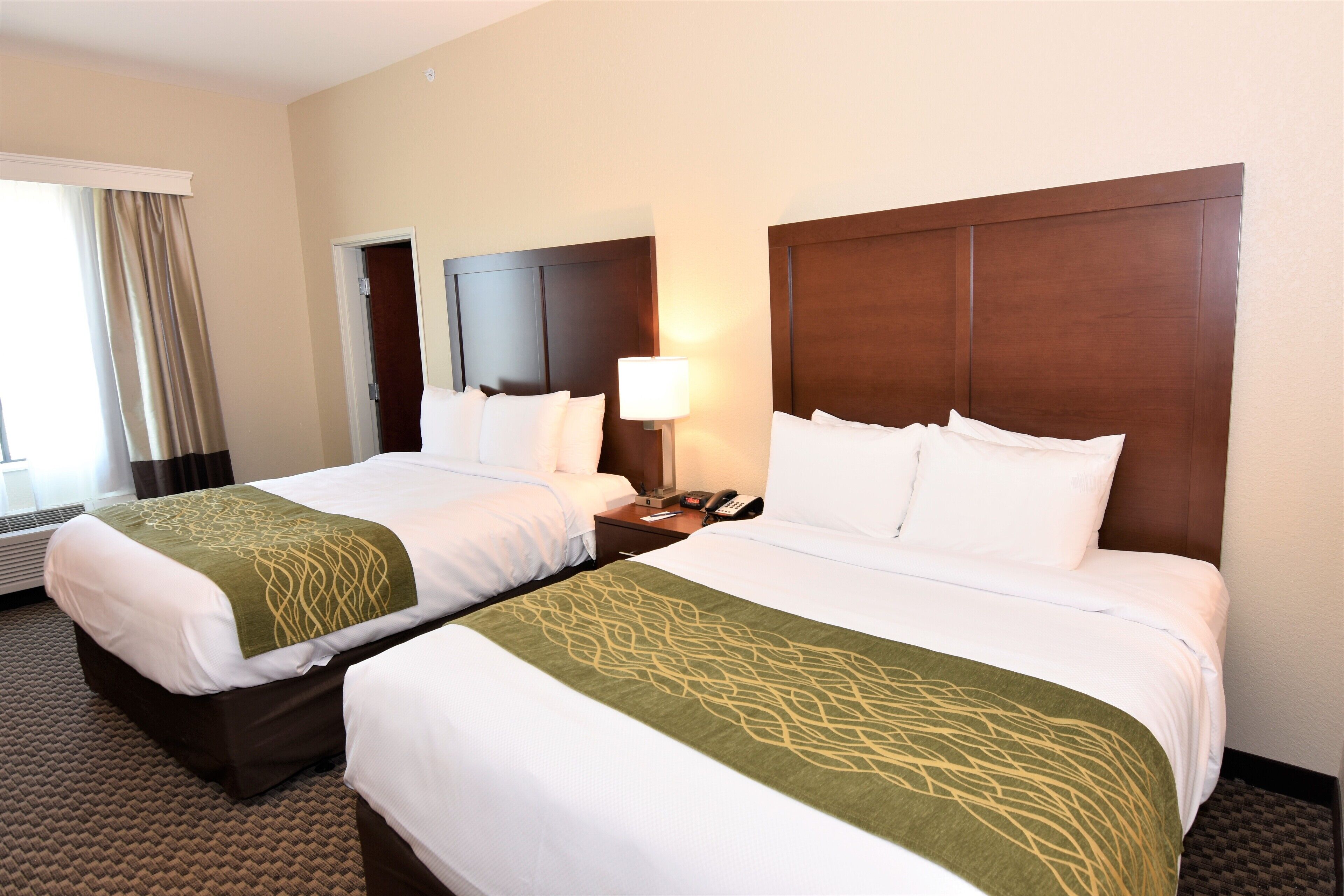 Two double beds with white linens and green decorative throws, a bedside table with a lamp, and a telephone.
