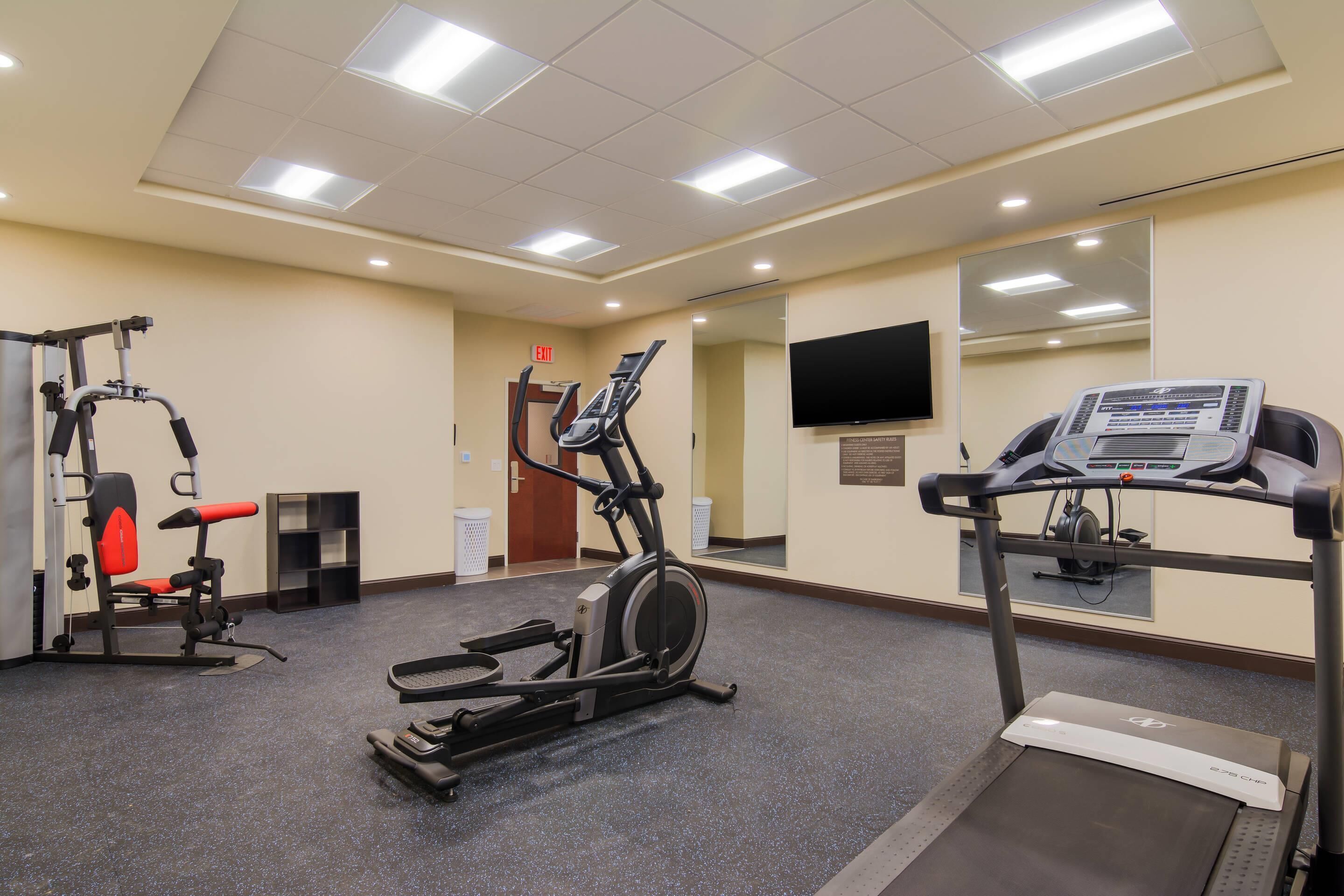 A gym with exercise equipment, a treadmill, and a television on the wall.