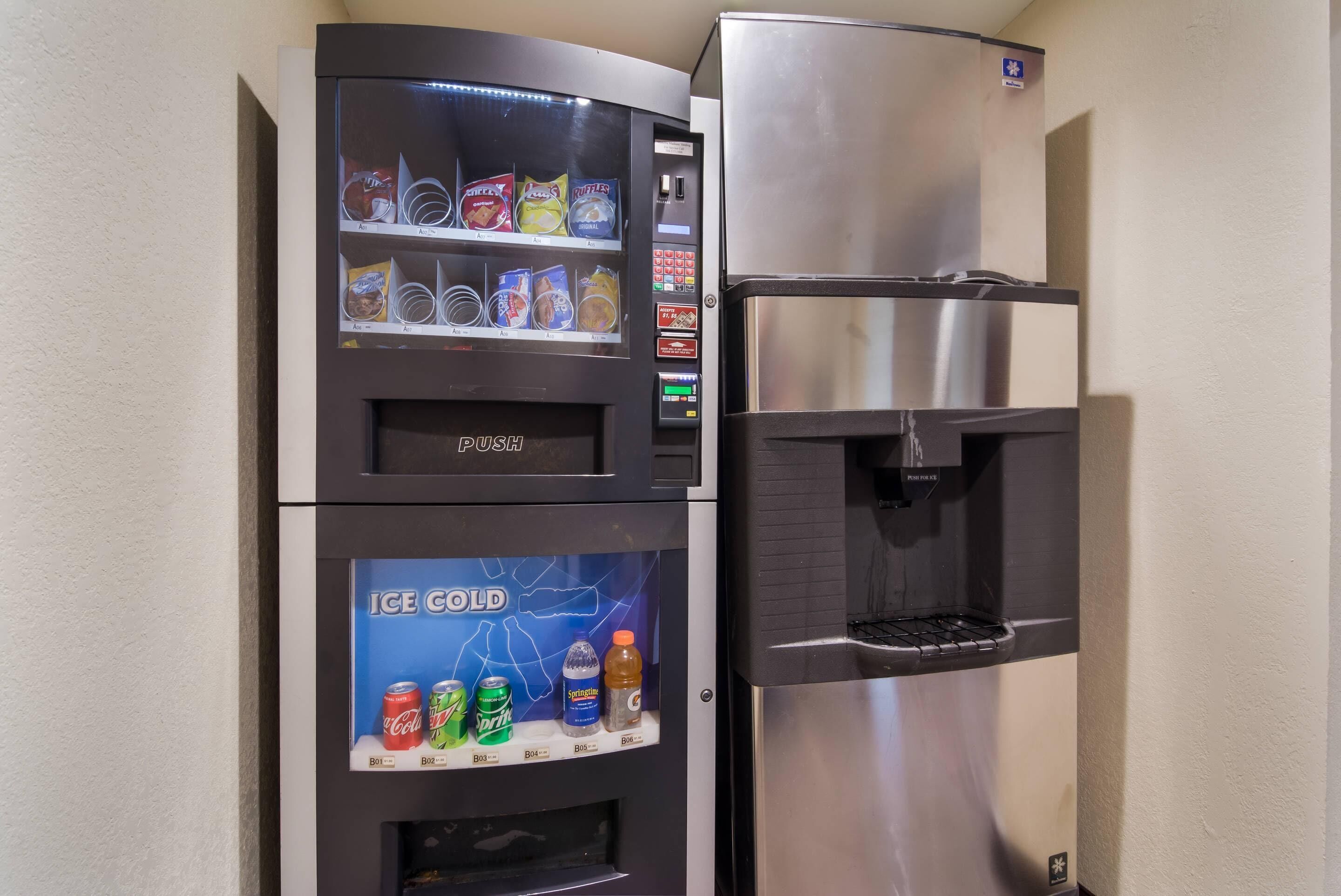 A vending machine with snacks and a water dispenser next to a stainless steel refrigerator.