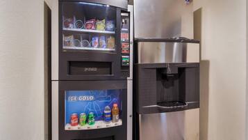 A vending machine with snacks and a water dispenser next to a stainless steel refrigerator.