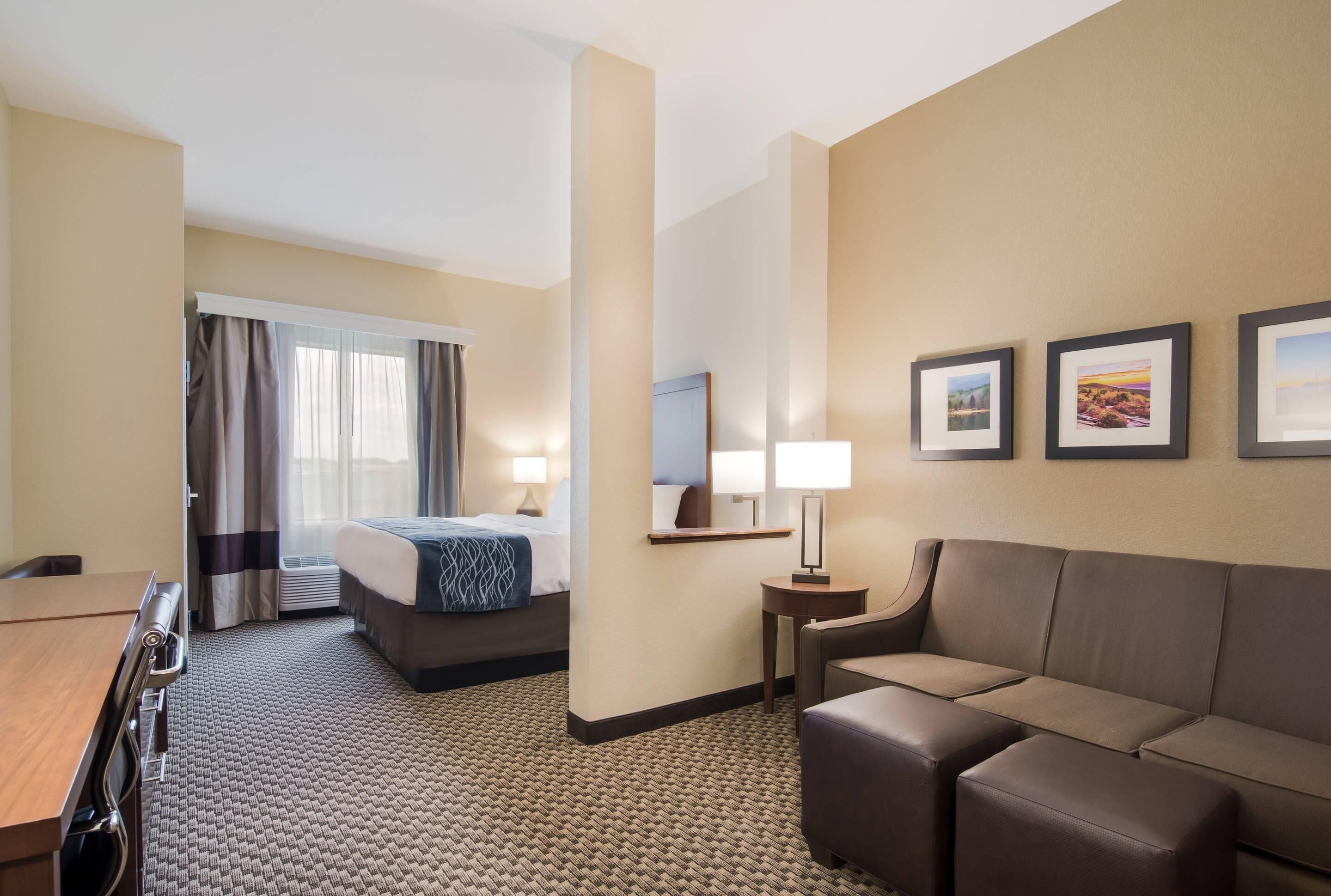 A hotel room with a bed, a sofa, a desk, a mirror, and framed pictures on the wall.