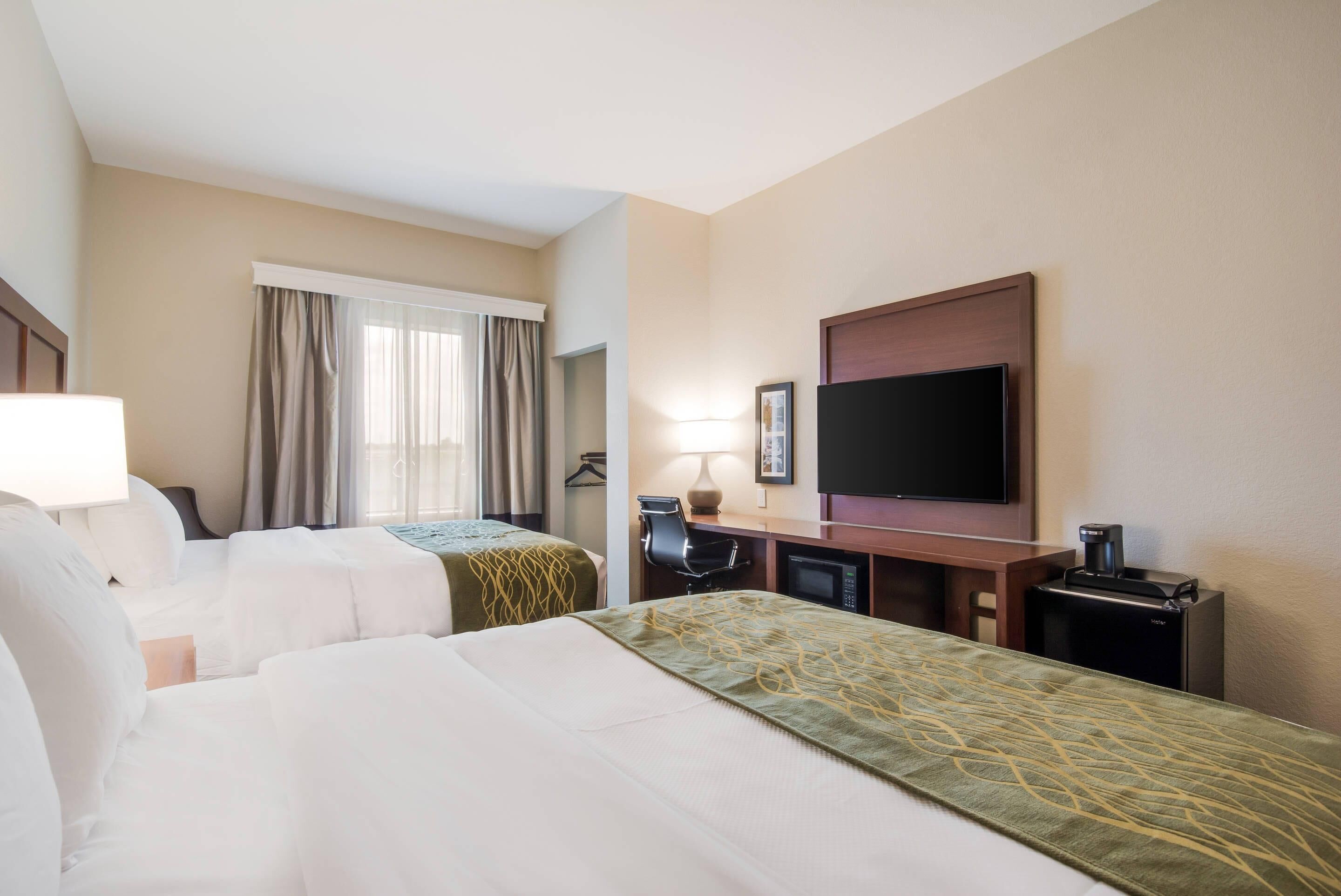 A hotel room with two beds, a desk with a chair, a television, a coffee maker, and a window with curtains.
