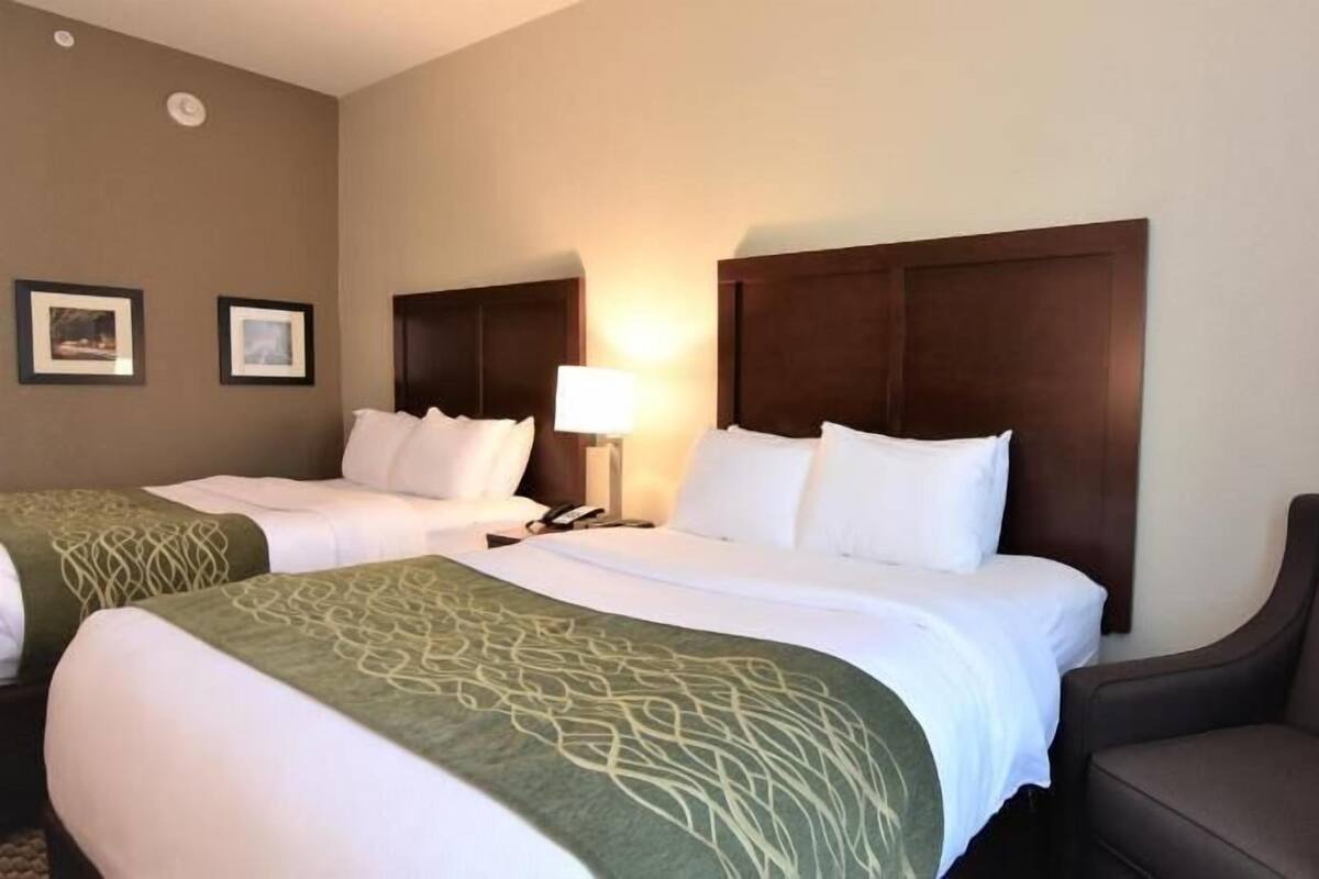 Ein Hotelzimmer mit zwei Betten, einem Sessel, einer Lampe und gerahmten Bildern an der Wand.