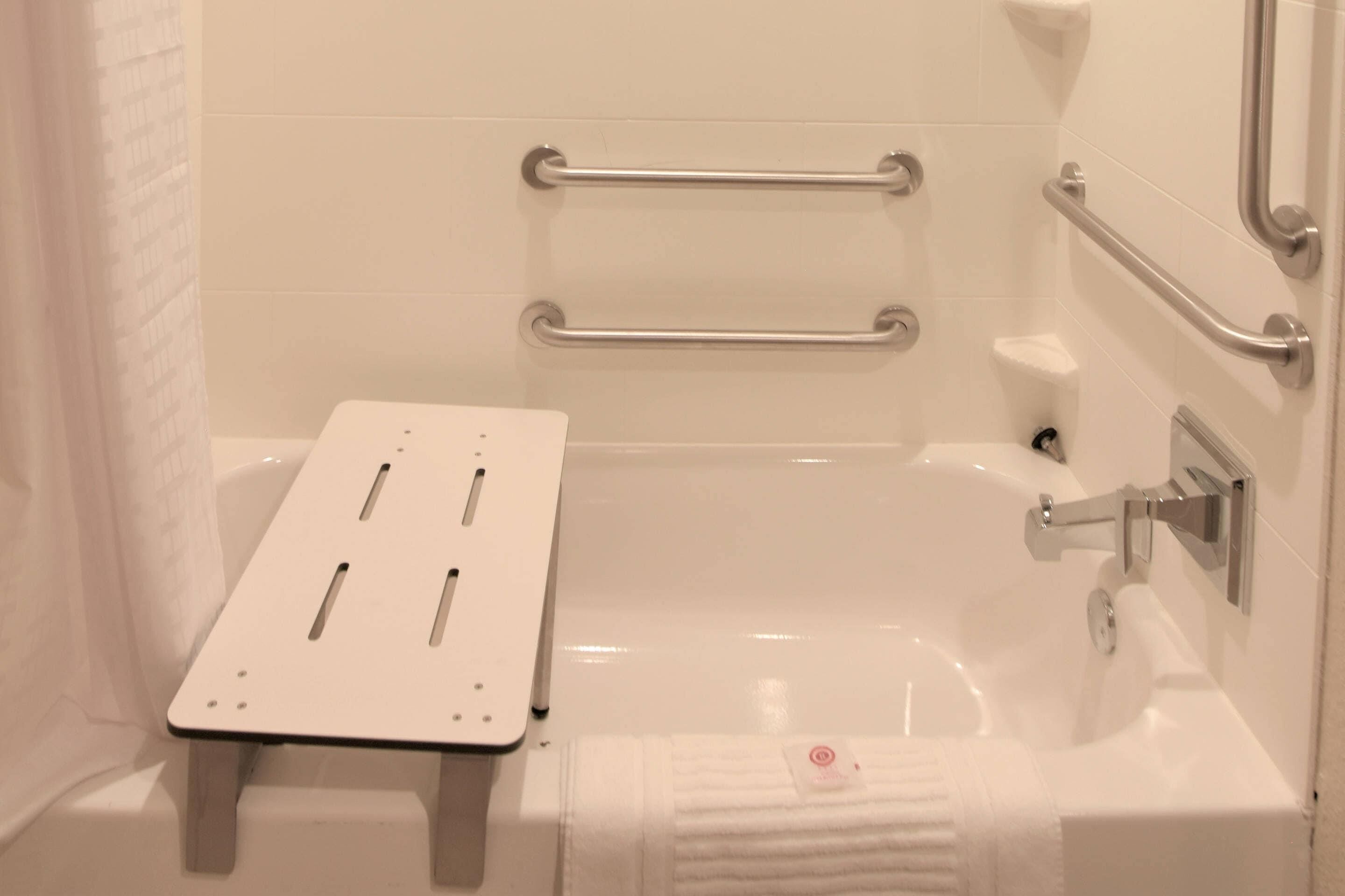 A bathroom with a bathtub, grab bars, a towel rack, and a shower curtain.