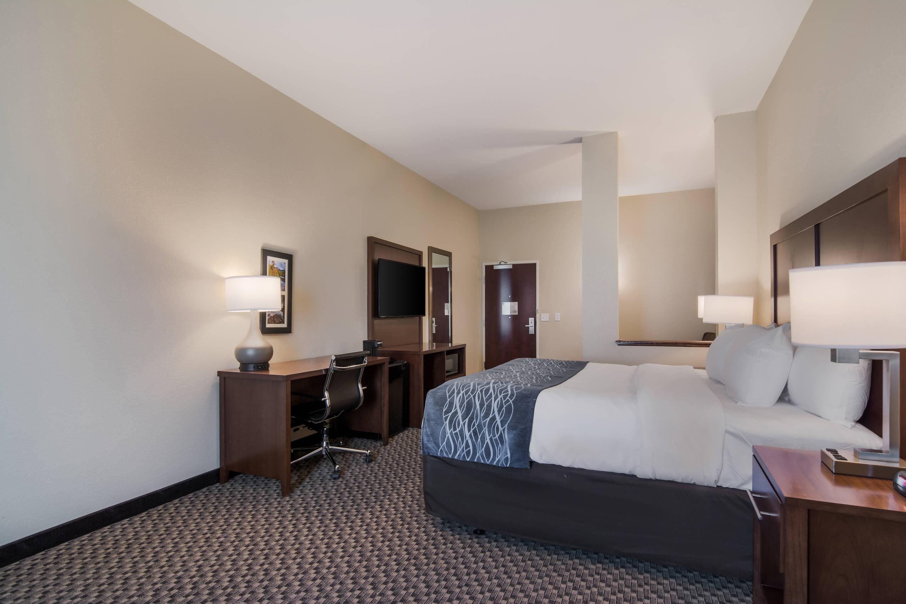 Una habitación de hotel con cama, escritorio, silla y dos lámparas.