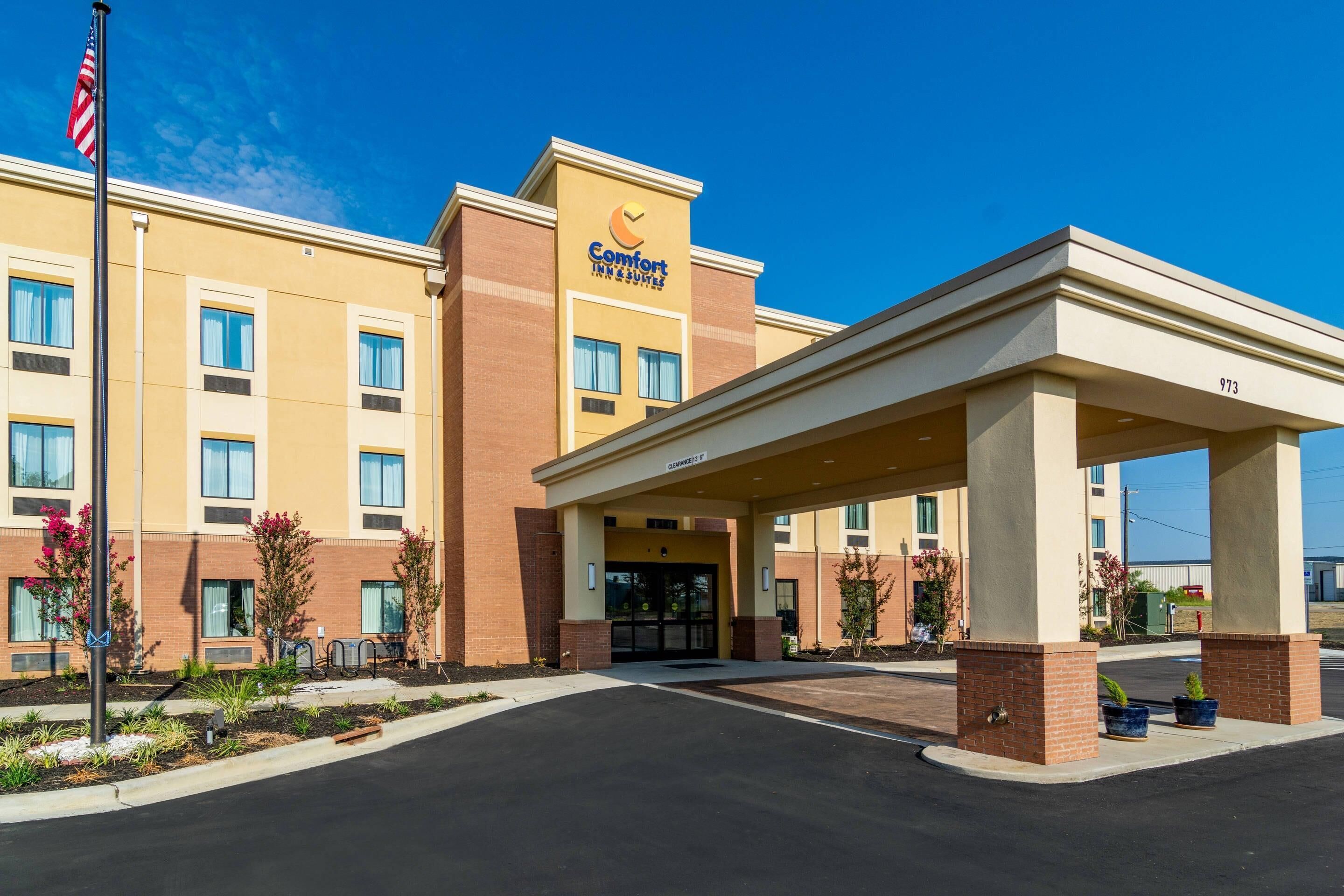 Edificio de Comfort Inn & Suites con un acceso cubierto, una bandera y un cielo azul despejado.