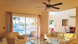 Una sala de estar con una mesa de centro de vidrio, dos sofás color beige y un ventilador de techo.