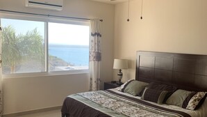 Un dormitorio con cama, ventilador de techo, ventana con vista al mar y aire acondicionado.
