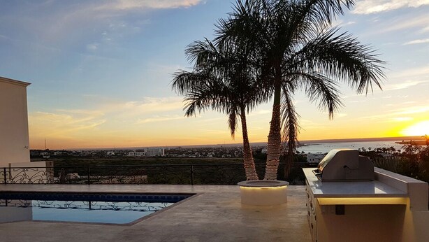 Una terraza en la azotea con piscina, zona de barbacoa y vistas al atardecer sobre la ciudad.
