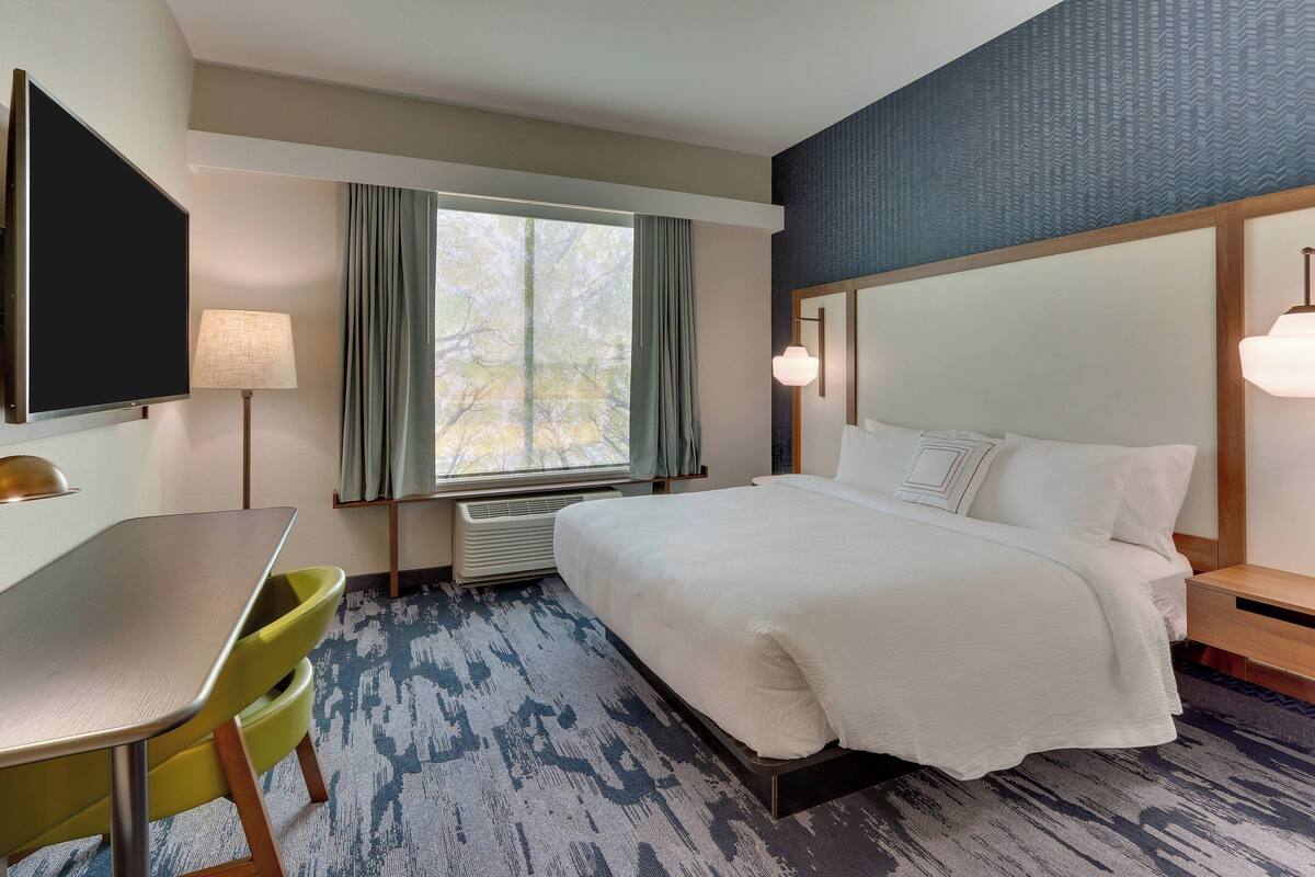 A hotel room with a bed, a desk, a chair, a TV, and a window with curtains.