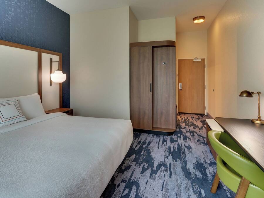 Una habitación de hotel con cama, escritorio, silla, armario y lámpara.
