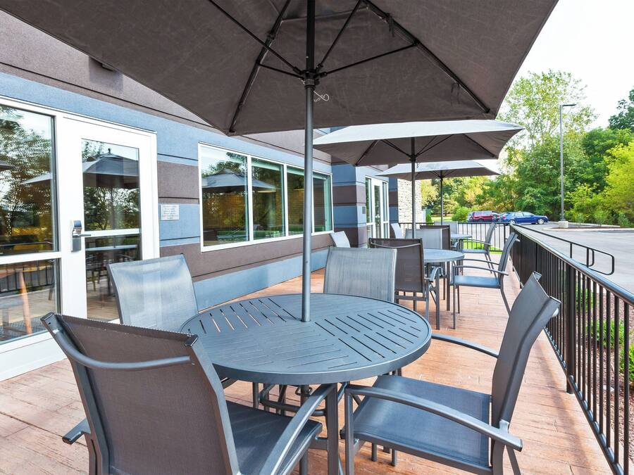 An outdoor patio with round tables and chairs, covered by large umbrellas, and a view of the street and greenery.