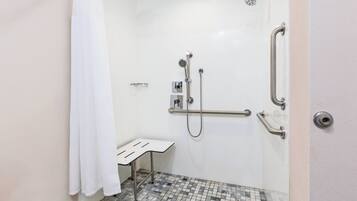 Un baño pequeño y blanco con ducha, barras de apoyo y un banco.