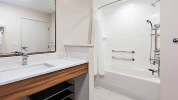 Un baño moderno con un lavabo blanco, tocador de madera, un espejo grande y una ducha a ras de suelo con puerta de cristal.