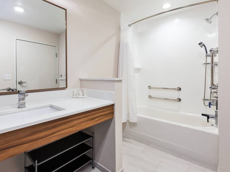 Un baño moderno con un lavabo blanco, tocador de madera, un espejo grande y una ducha a ras de suelo con puerta de cristal.