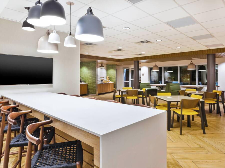 Un comedor moderno con una larga barra blanca, varias sillas e iluminación colgante.