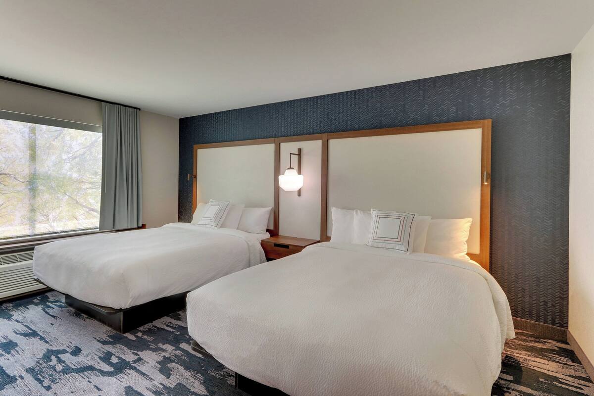 A hotel room with two beds, a large window, and a patterned carpet.