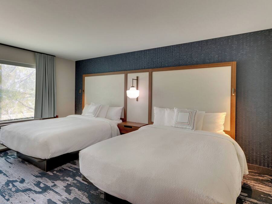 Habitación de hotel con dos camas, un ventanal grande y una alfombra estampada.