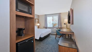Una camera d'albergo con un letto, una scrivania, una sedia, un forno a microonde, una macchina del caffè e un piccolo frigorifero.