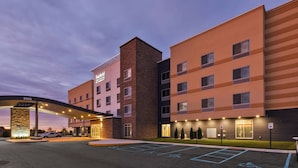 Cet hôtel présente un design moderne, avec une façade en briques et de nombreuses fenêtres. On peut voir un espace de stationnement couvert où une voiture est garée.