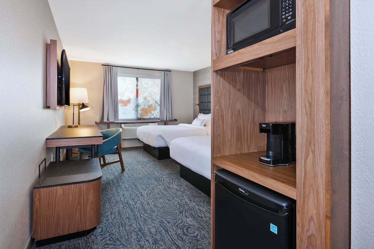 Ein Hotelzimmer mit Schreibtisch, zwei Betten, einer Mikrowelle, einer Kaffeemaschine und einem Kühlschrank.