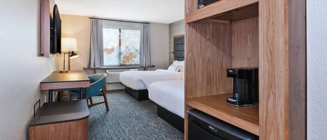 A hotel room with a desk, two beds, a microwave, a coffee maker, and a refrigerator.