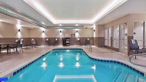 Une piscine dont le bord est revêtu de carreaux, entourée de chaises et de tables, et dont le plafond est doté d’un éclairage encastré.