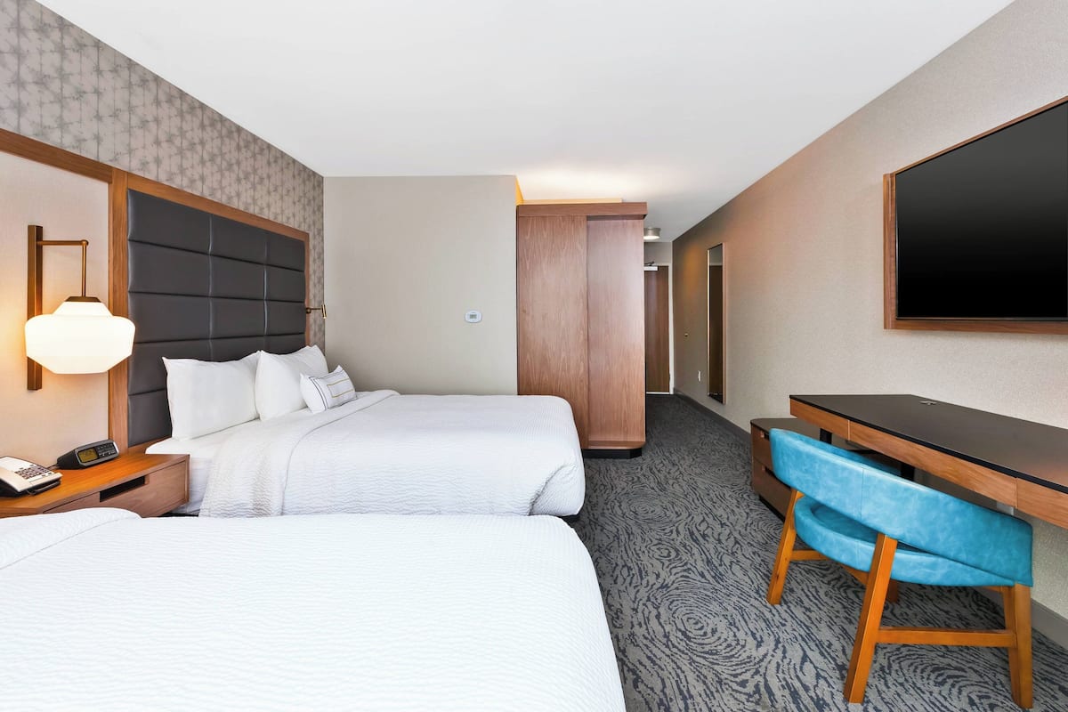 Ein Hotelzimmer mit zwei Betten, einem Schreibtisch, einem Sessel, einem Fernseher und einem Kleiderschrank.