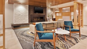 Un hall d’hôtel moderne avec un mur d’accent en pierre, une cheminée, un téléviseur à écran plat et des meubles en bois.