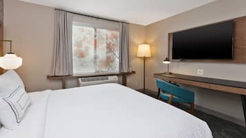 Habitación de hotel con una cama grande, un escritorio, una silla, un televisor de pantalla plana y un ventanal con cortinas.