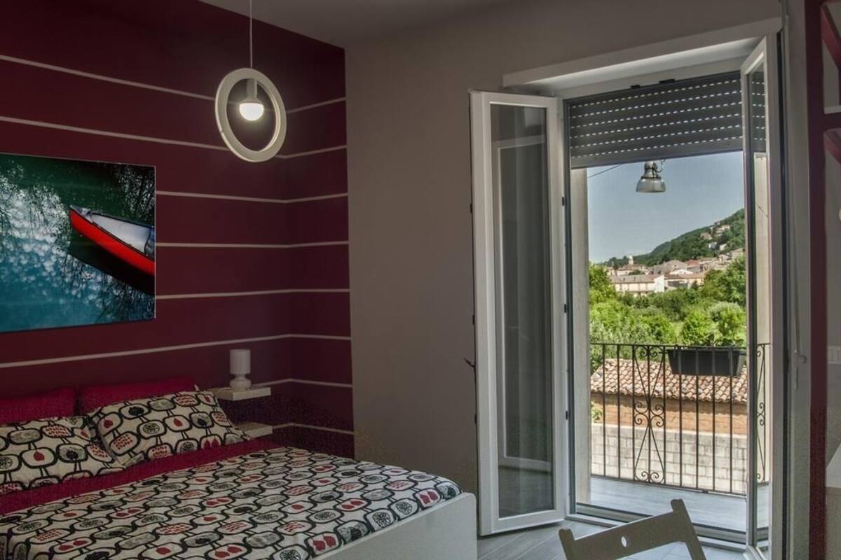 Une chambre à coucher avec un lit, un tableau et un balcon donnant sur la ville et les collines.