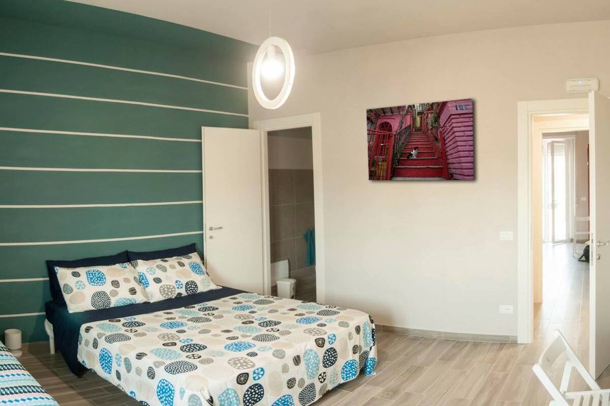 Une chambre à coucher avec un lit, une porte donnant sur une salle de bain et un tableau accroché au mur.