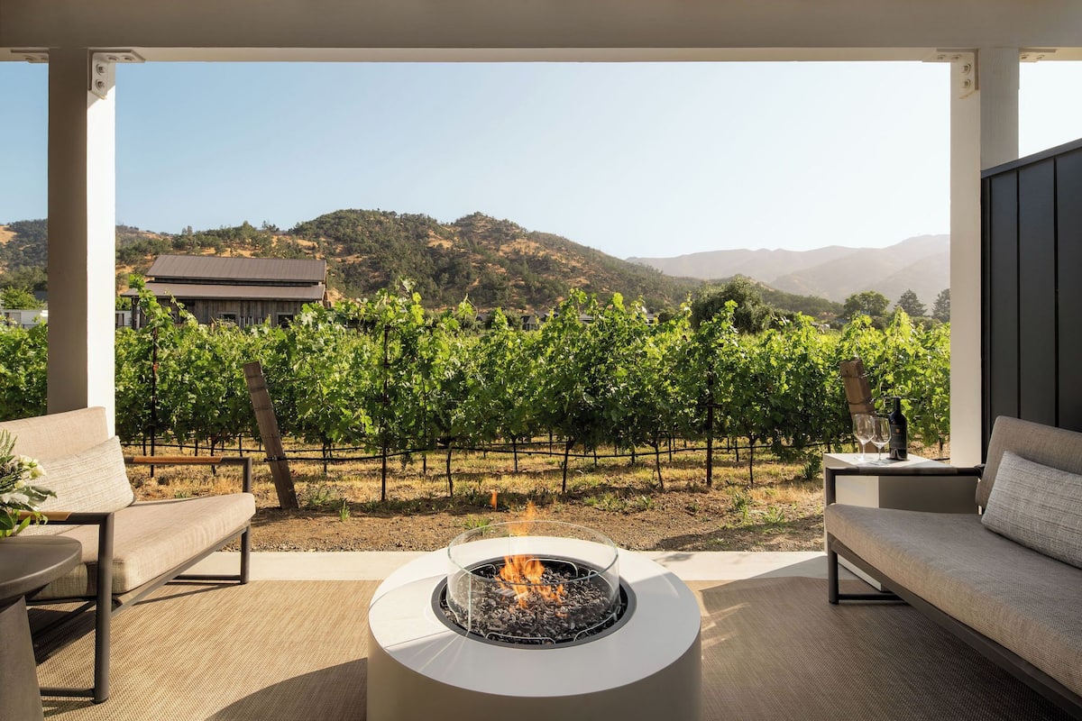 Eine Terrasse mit Feuerstelle, Sitzgelegenheiten im Freien und Blick auf einen Weinberg.