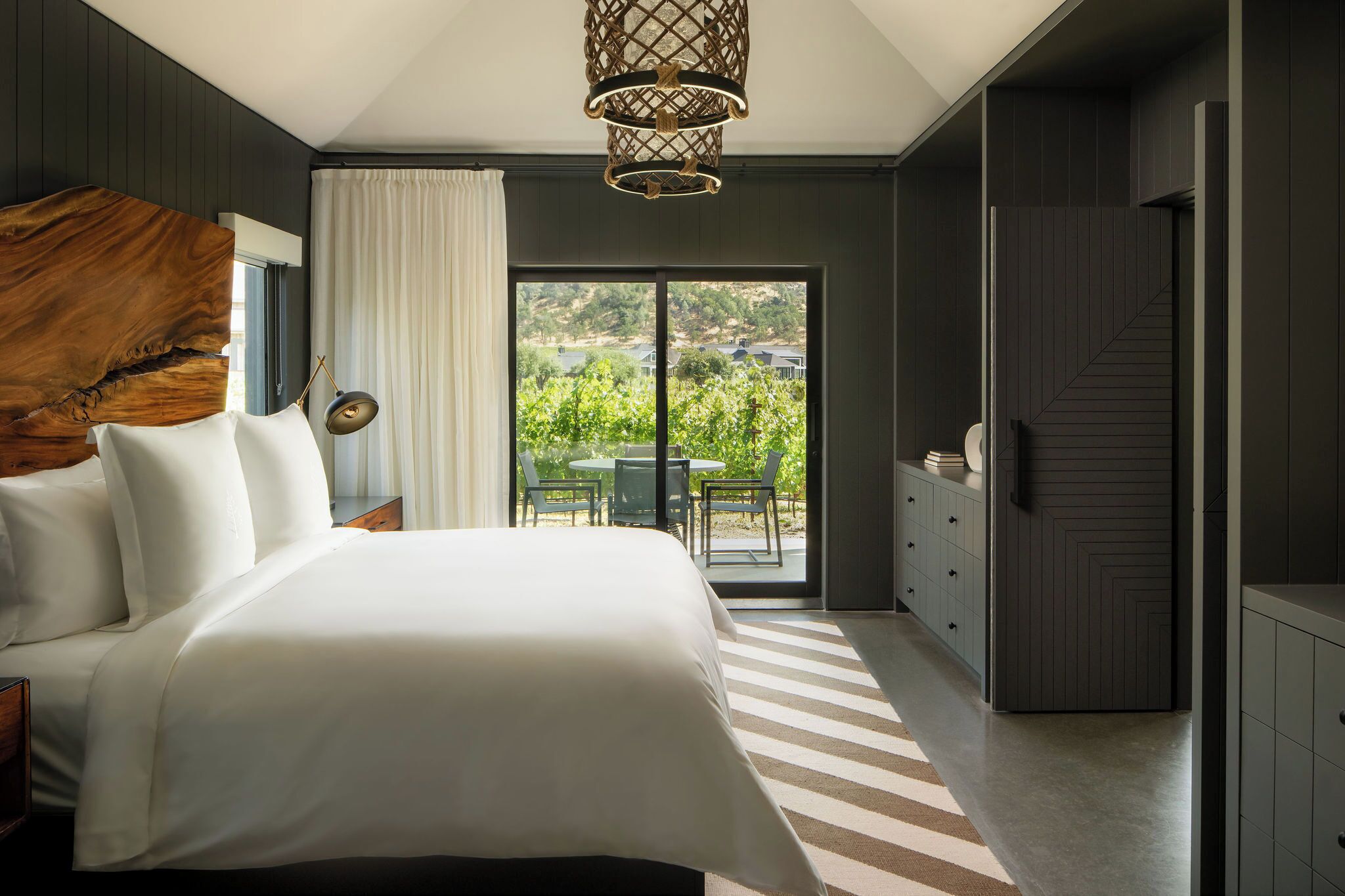 A bedroom with a large bed, a view of a garden through a sliding door, and a modern chandelier.