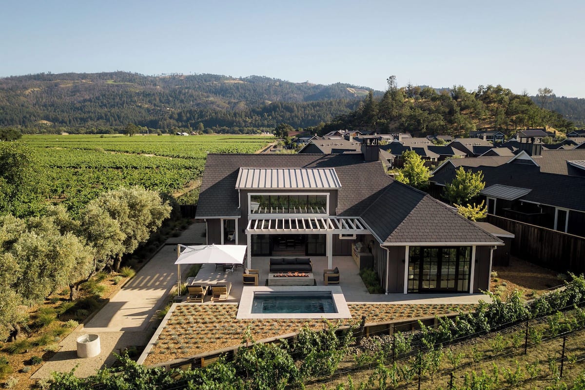 Ein modernes Haus mit Pool, Terrasse und einem Weinberg im Hintergrund.