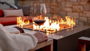 Eine Person sitzt an einem Tisch mit einem Glas Rotwein, einem Feuerkorb und Blick auf die Hügel im Hintergrund.
